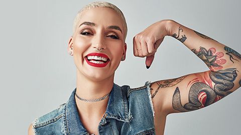 Eine Frau zeigt ihren Bizeps in die Kamera als ein Zeichen der Stärke und lacht dabei