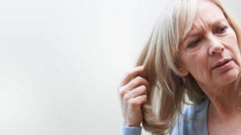 Eine Frau fässt sich in ihre Haare als Zeichen des Haarausfalls