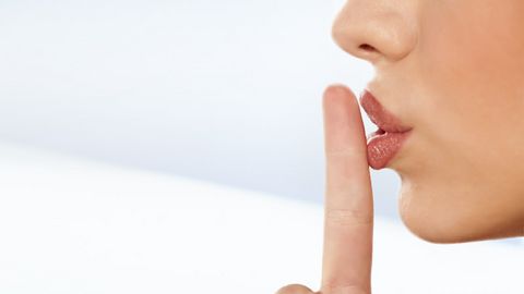 Eine Frau hält ihren Finger vor dem Mund und zeigt damit 